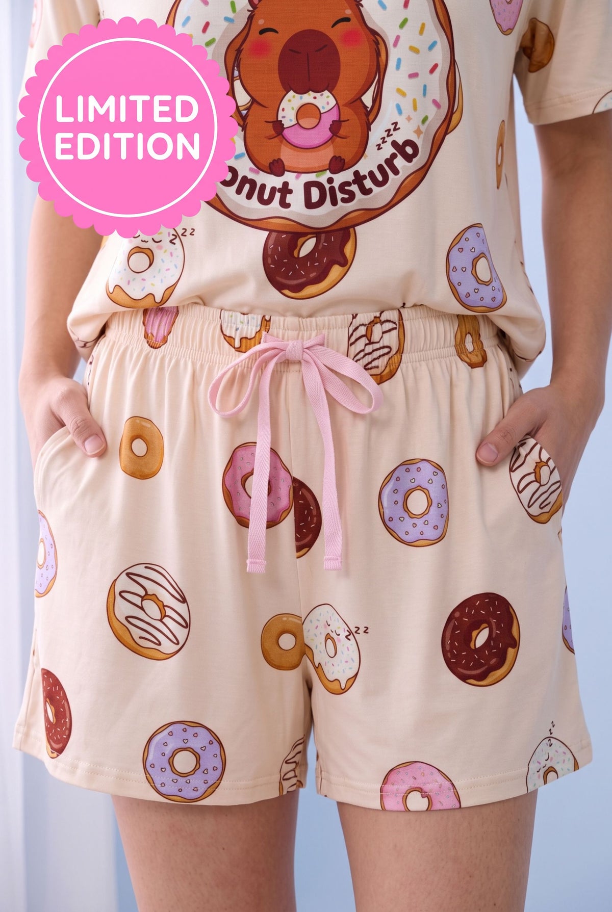 Donut Disturb bamboo pyjama shorts in cream with a scattered sleeping doughnut print, pink drawstring bow and side pockets.
