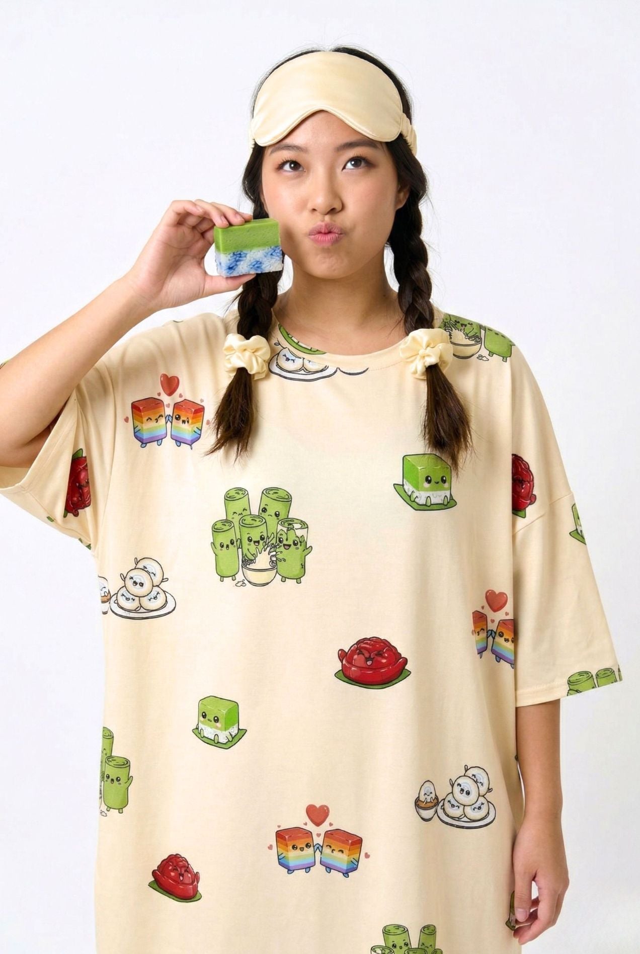 Woman holding a piece of kueh wearing the Kueh-zy Medley cream kueh print sleep tee and sleep mask