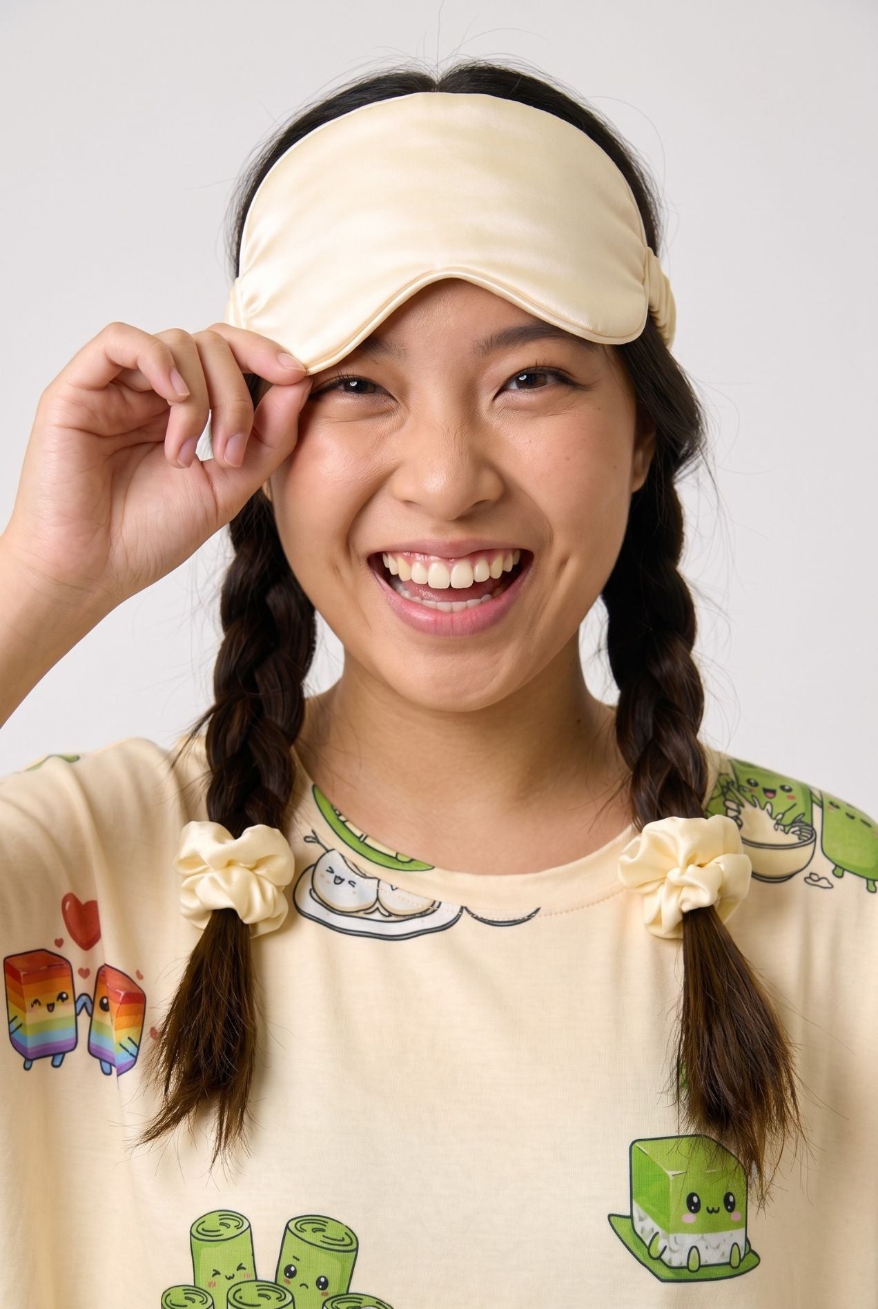Woman lifting a cream Kueh-zy Medley sleep mask off one eye with matching kueh print sleep tee and scrunchies