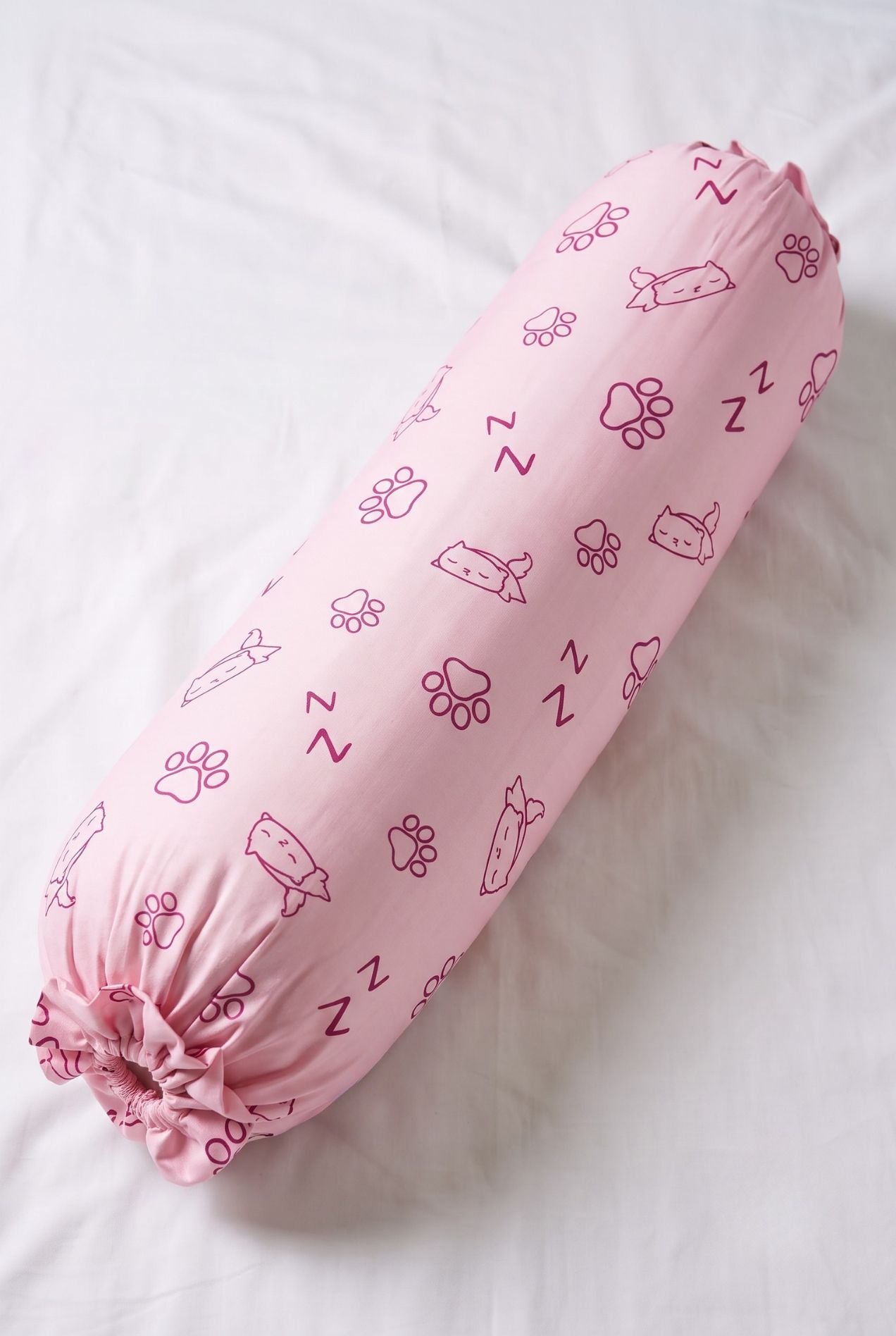 Paws & Snooze bamboo bolster cover in pink cat and paw print, flat lay on white bedding