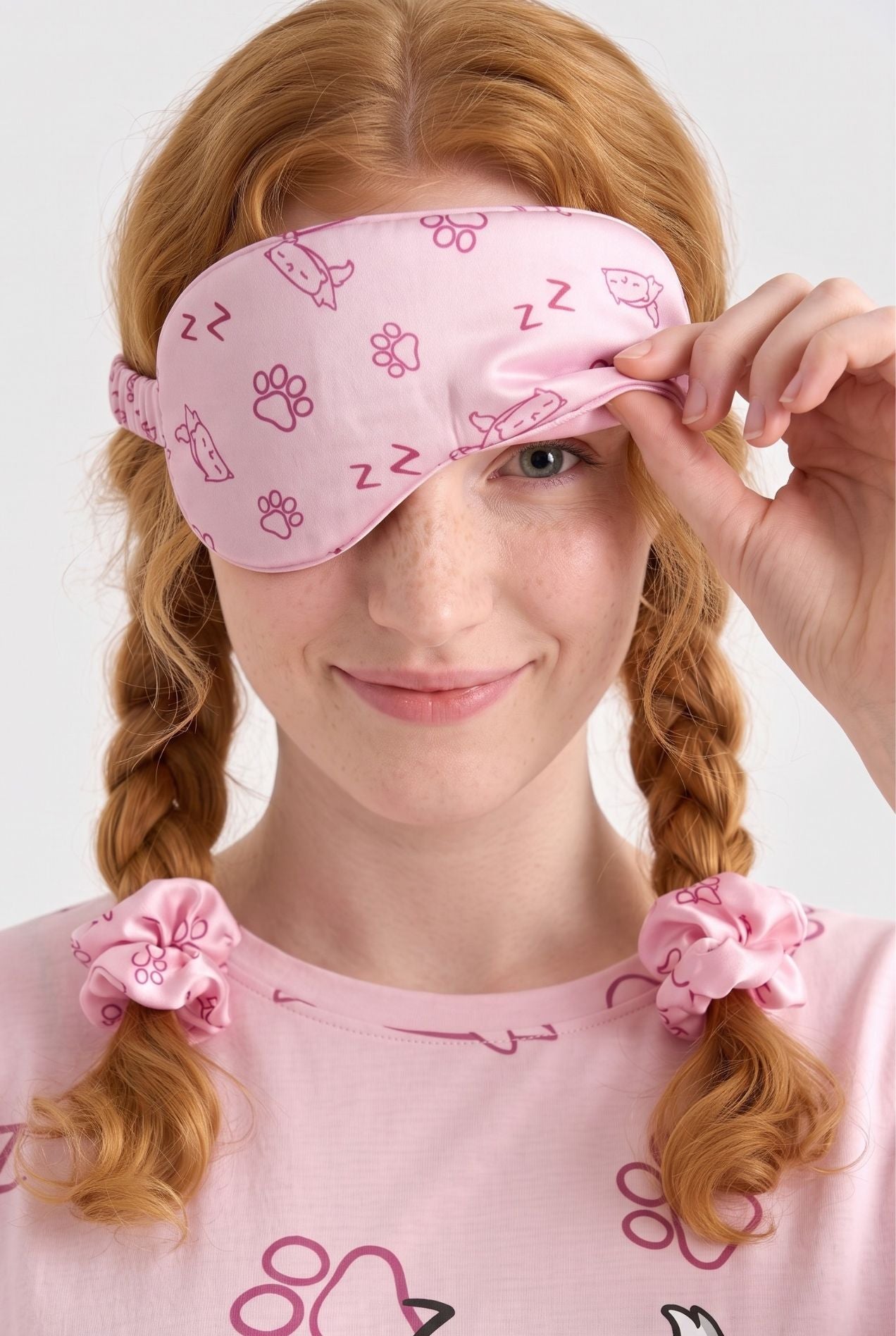 Woman lifting a Paws & Snooze bamboo sleep mask in pink cat print off one eye