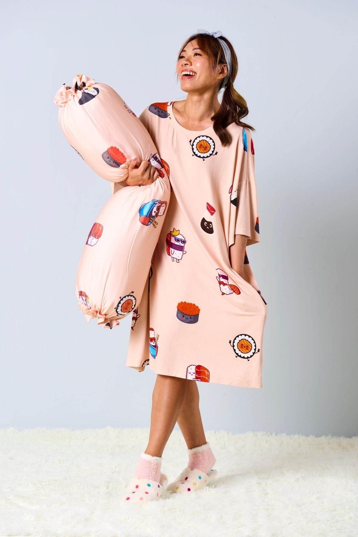 Woman wearing a salmon colored dress with food-themed designs, holding a pink bolster with cartoon characters.